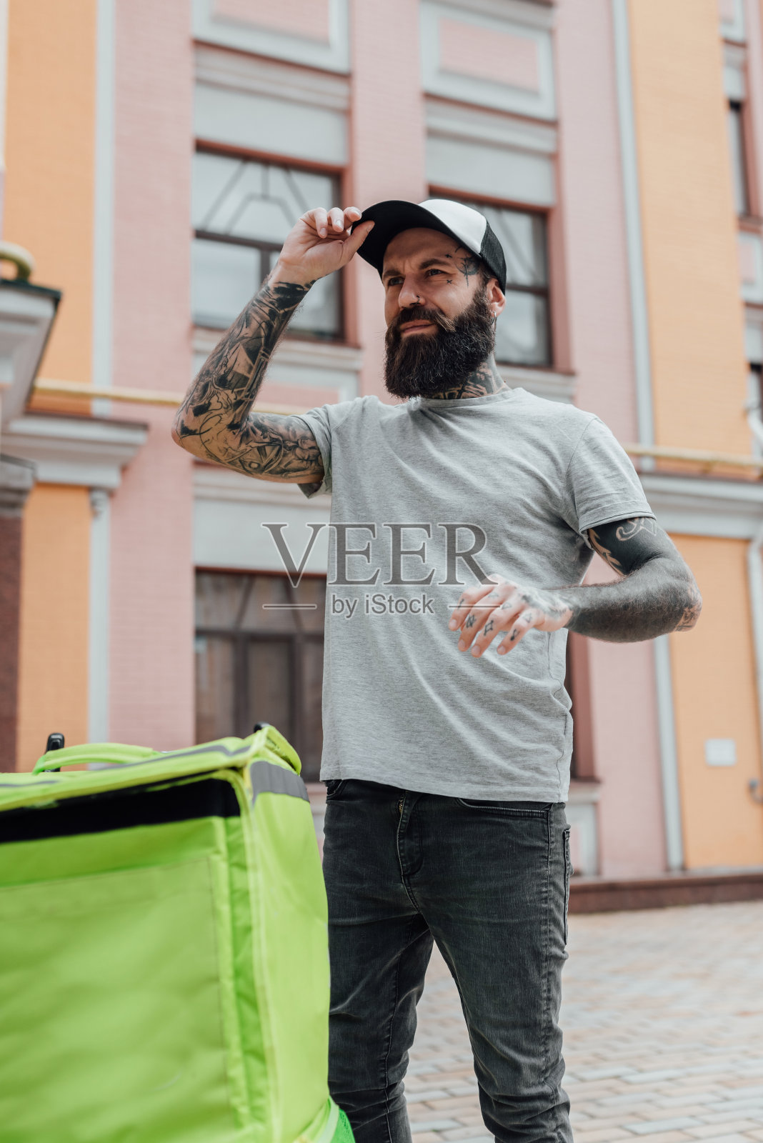 随时可以上菜。残忍时尚的送餐员戴着帽子向一边看,背着背包站在户外,准备送完食物后走。快递、派送的服务理念照片摄影图片