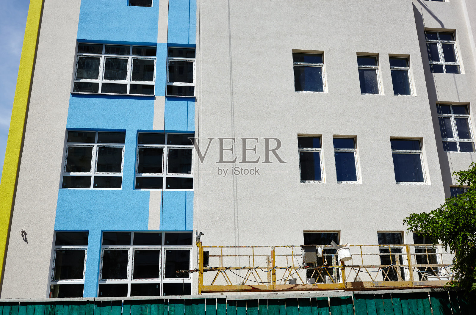 幼儿园大楼建设的进度。建筑外立面的现代装饰。施工现场悬挂脚手架平台或窗户清洁摇篮系统照片摄影图片