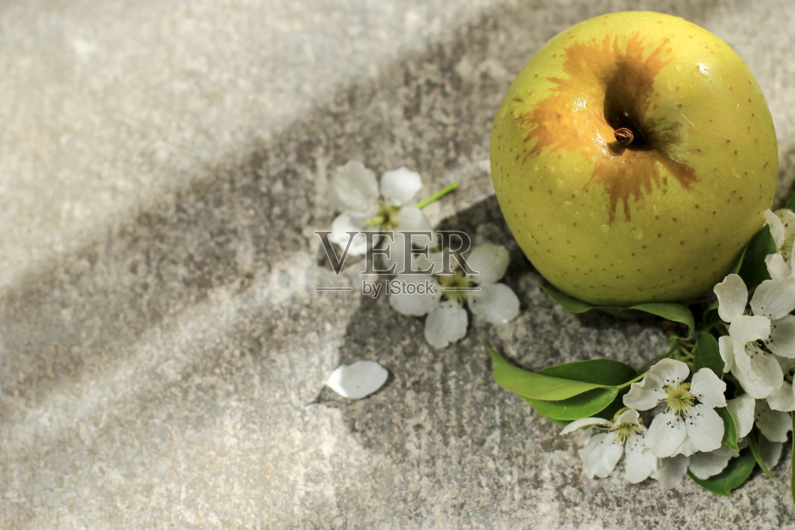 一个成熟的黄色的苹果和苹果树花在灰色的混凝土背景与光影。春天的概念,园艺,收获,健康食品。副本的空间。照片摄影图片