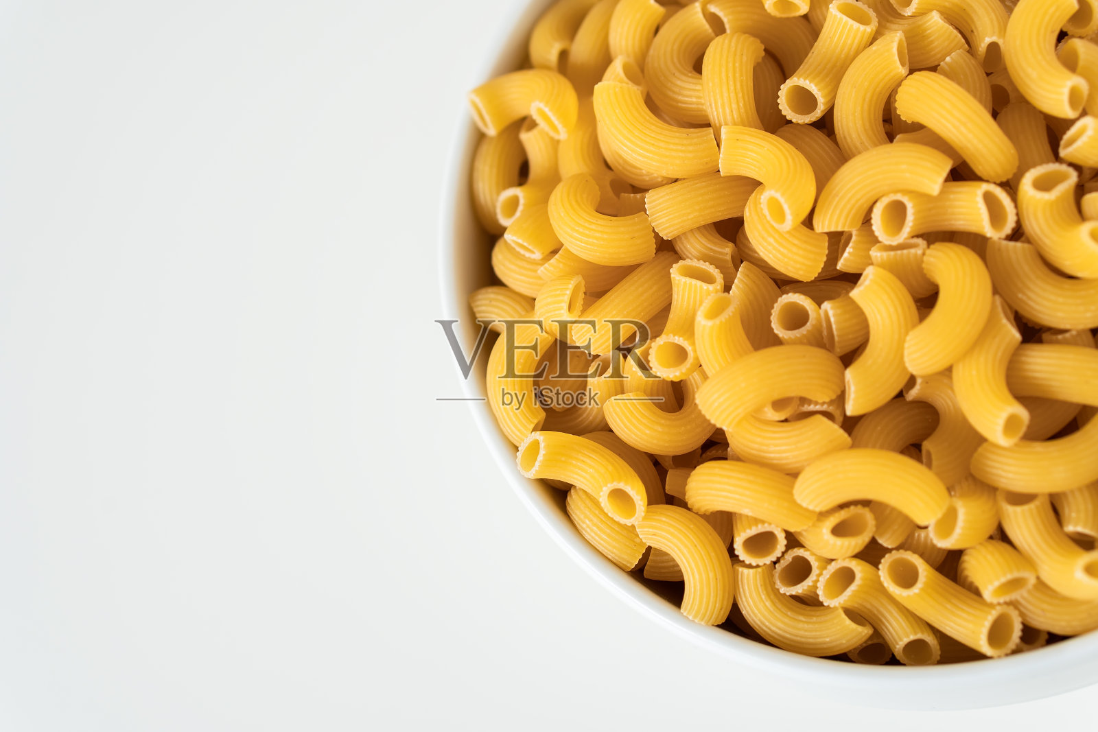 生的,干的,生的手肘通心粉通心粉在白色的背景。适合做罗勒、蕃茄、香蒜沙司自制的新鲜意大利食品,有机全麦素食面条,健康的一餐照片摄影图片