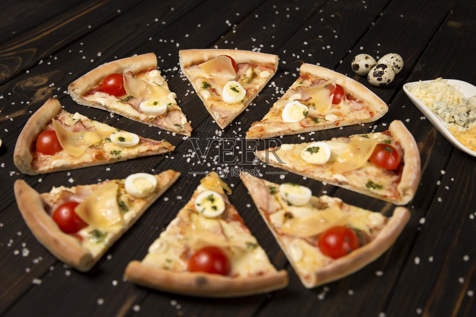 切片披萨配番茄、香蒜沙司、培根、马苏里拉奶酪和帕玛森奶酪。背景是海盐,奶酪托盘和鹌鹑蛋。照片摄影图片