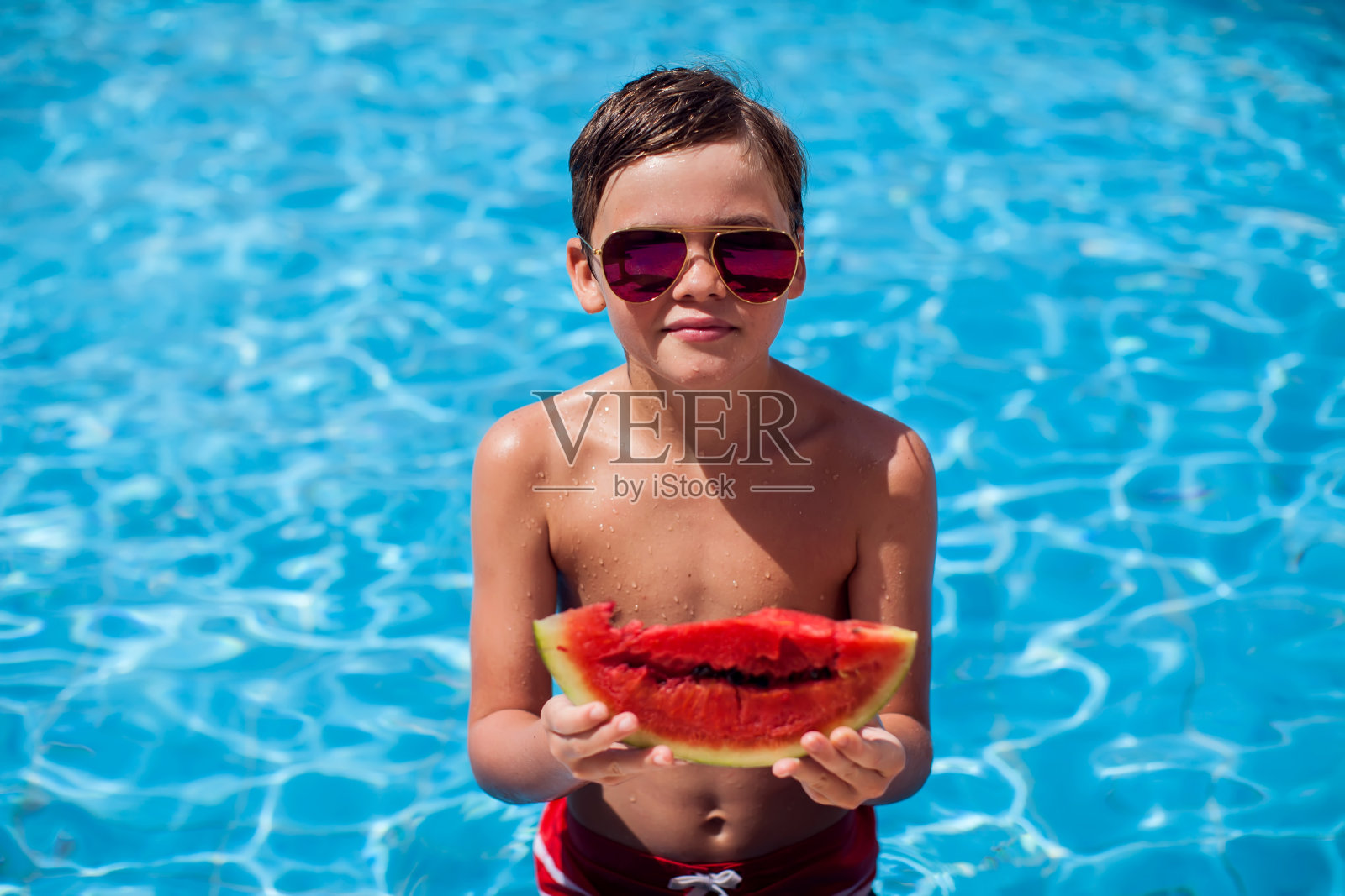 一个小男孩在游泳池边吃西瓜。童年、夏季和假期的概念照片摄影图片