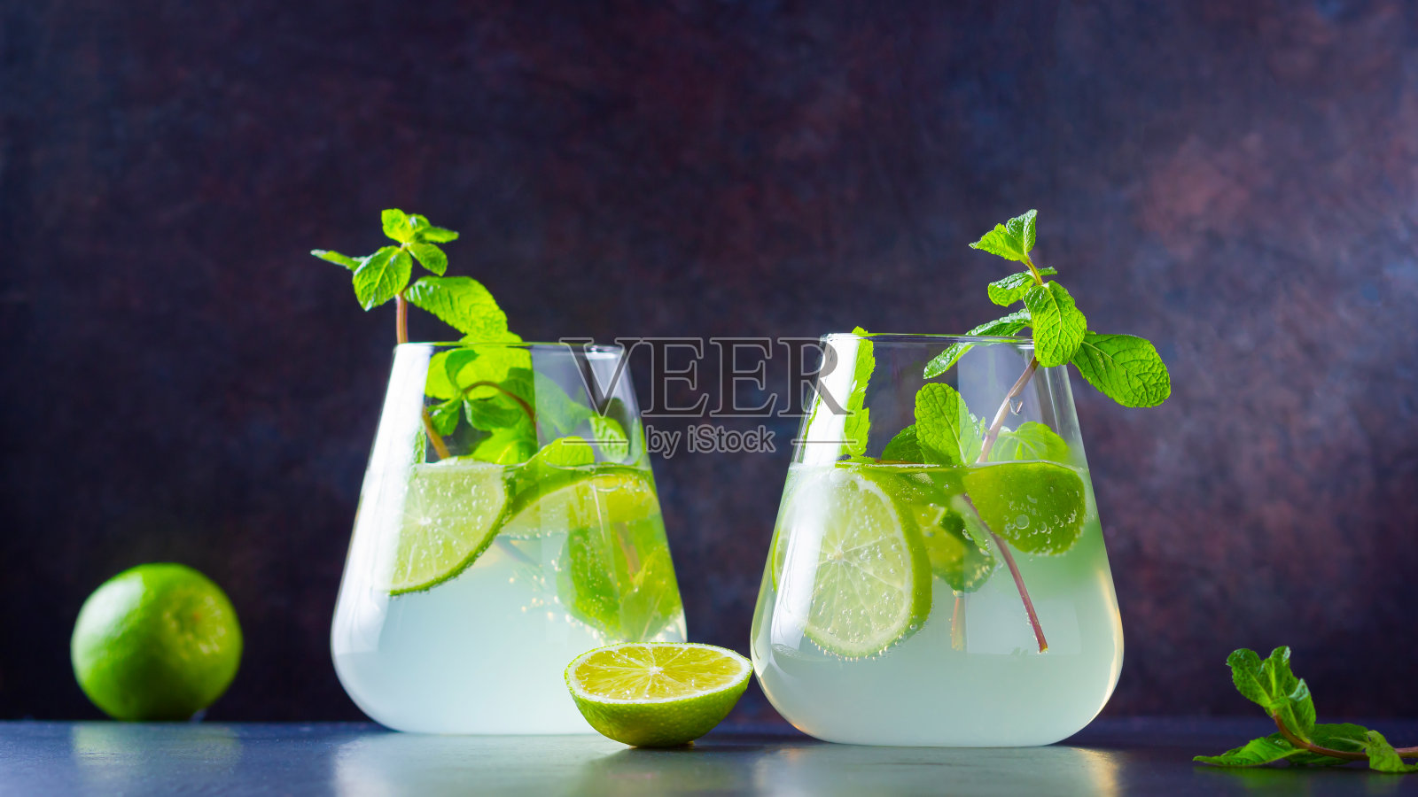 莫吉托鸡尾酒,柠檬和薄荷杯。两杯莫吉托,深色背景。清新的薄荷鸡尾酒配青柠。注入水照片摄影图片