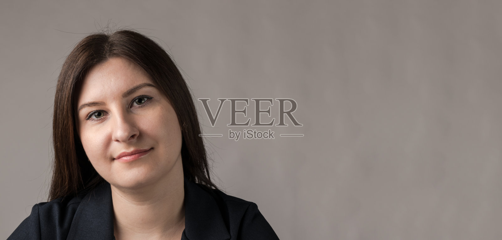 年轻美丽的黑发女子微笑着看着照相机在灰色的背景。照片摄影图片