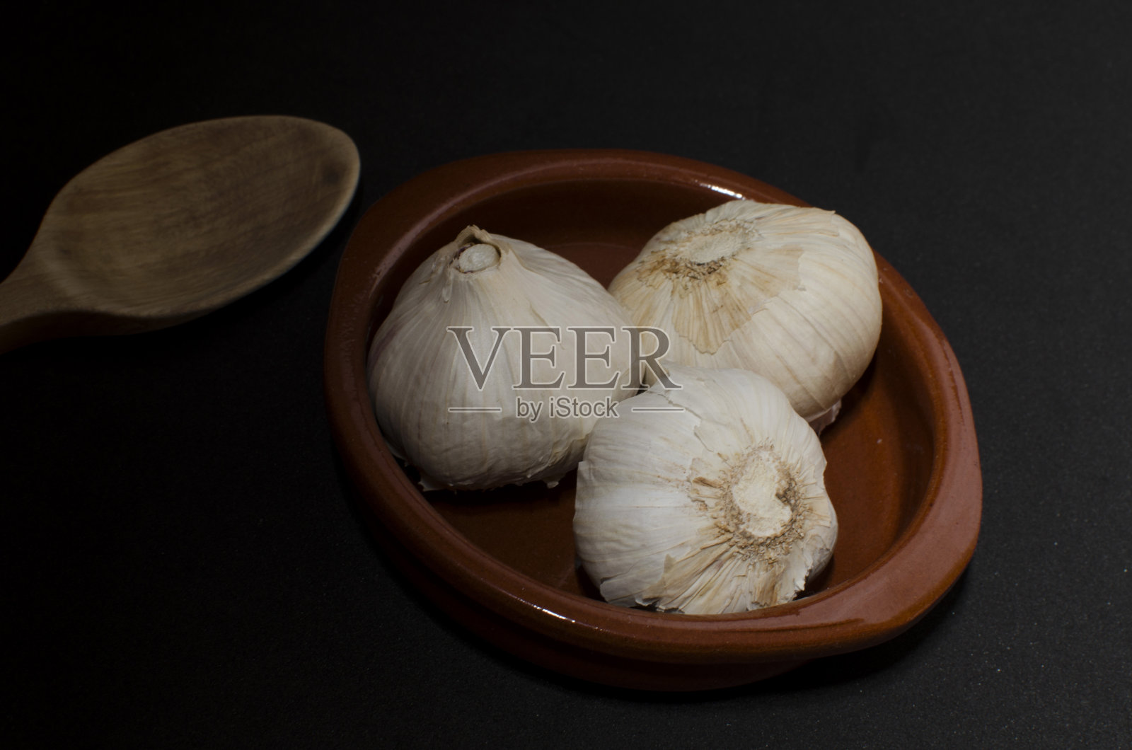 三个大蒜在砂锅和木勺照片摄影图片