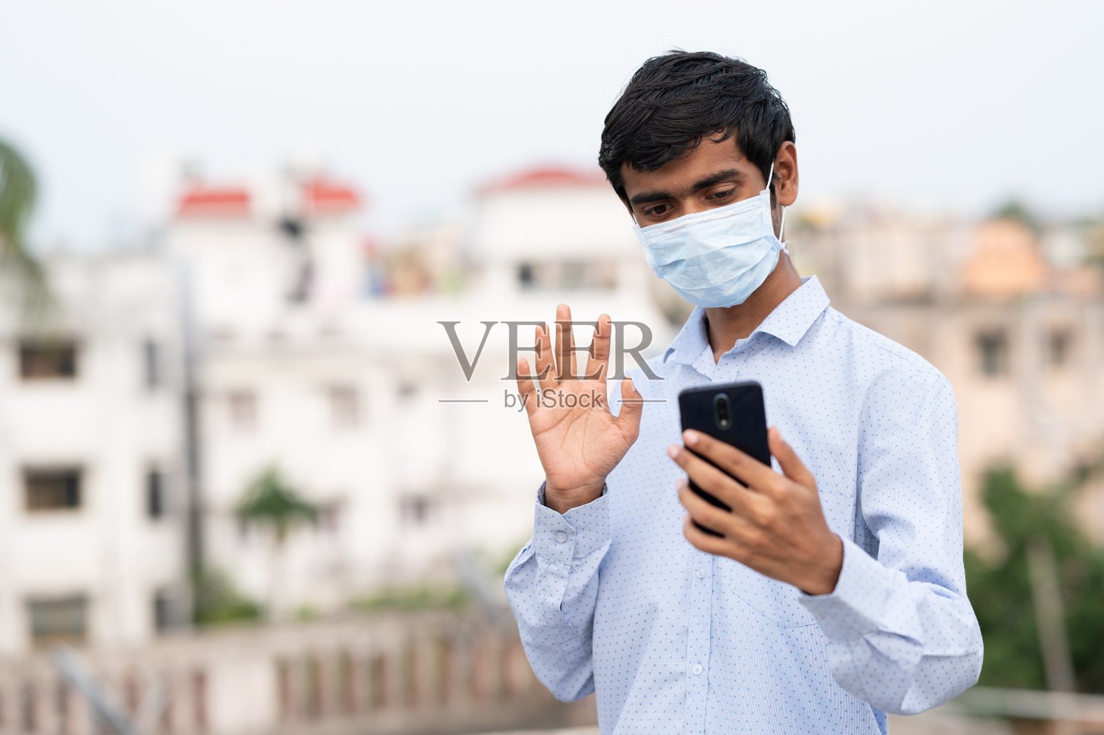 年轻的印度/南亚男子戴着医用口罩,使用手机自拍。照片摄影图片
