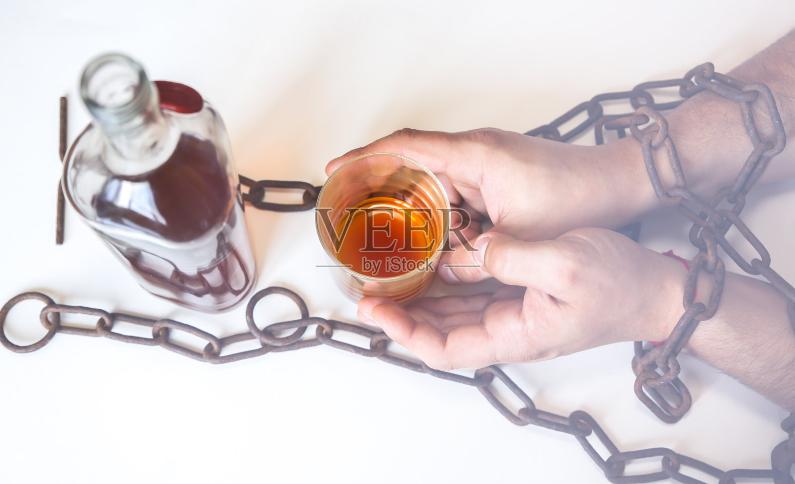 男人拿着生锈的链条,靠近酒瓶。沉迷酒精,危险的习惯。照片摄影图片