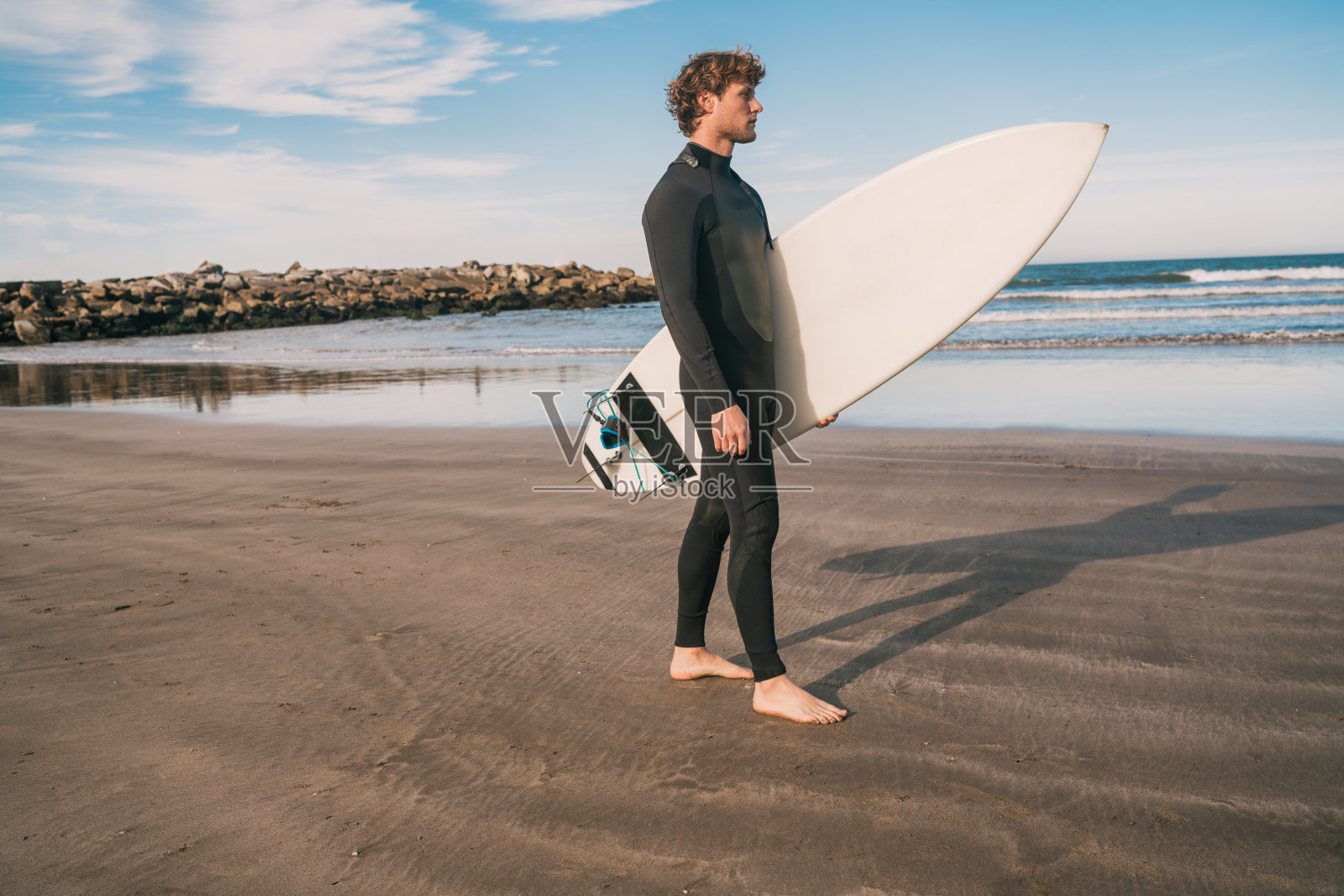 冲浪者拿着冲浪板站在海里。照片摄影图片