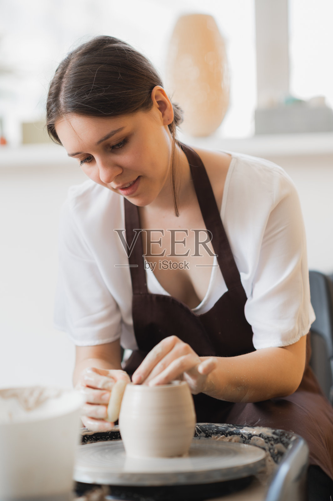 年轻的女陶工的特写镜头与海绵保持它靠近旋转的陶罐,而塑造形式的锅在工作期间照片摄影图片