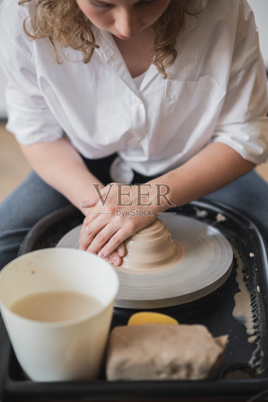 女孩用粘土做陶器。她用扭曲的陶轮用白粘土制作陶瓷制品照片摄影图片