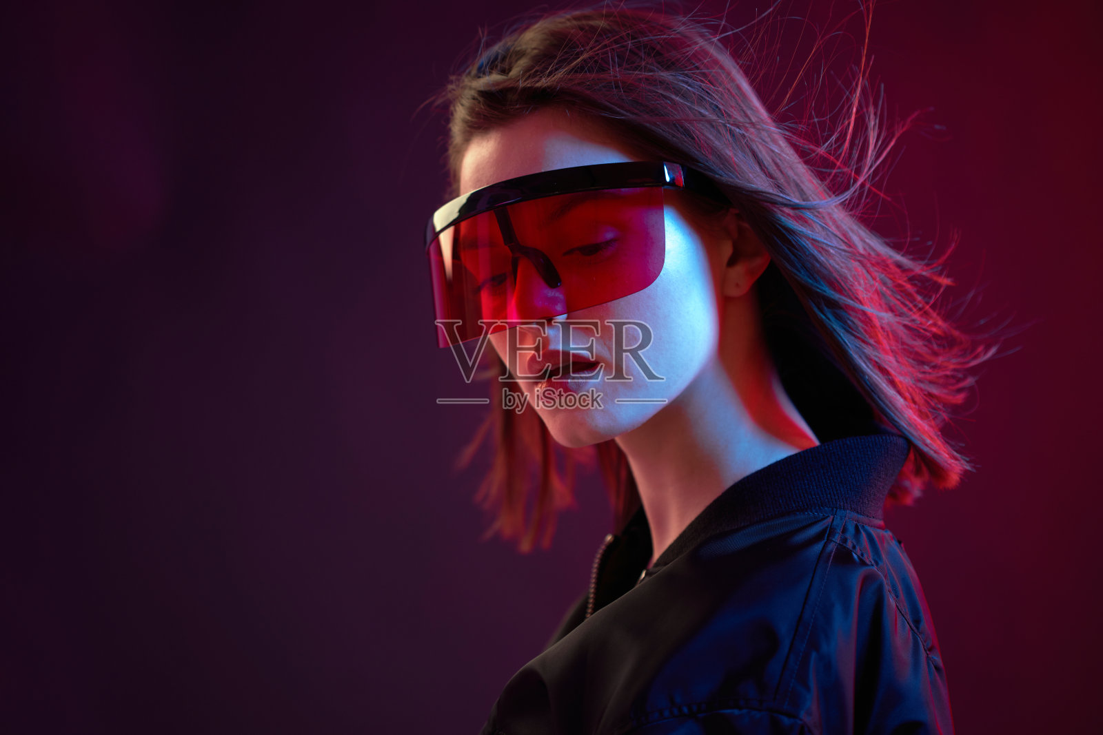 一个很酷的女孩的肖像,穿着黑色短夹克,戴着墨镜,背景是霓虹灯。照片摄影图片