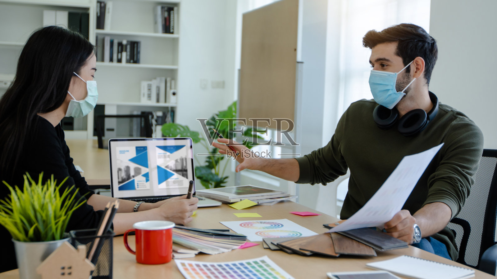 创意人士和平面设计师戴着口罩保护新冠病毒,在办公室讨论和计划为书籍封面选择颜色照片摄影图片