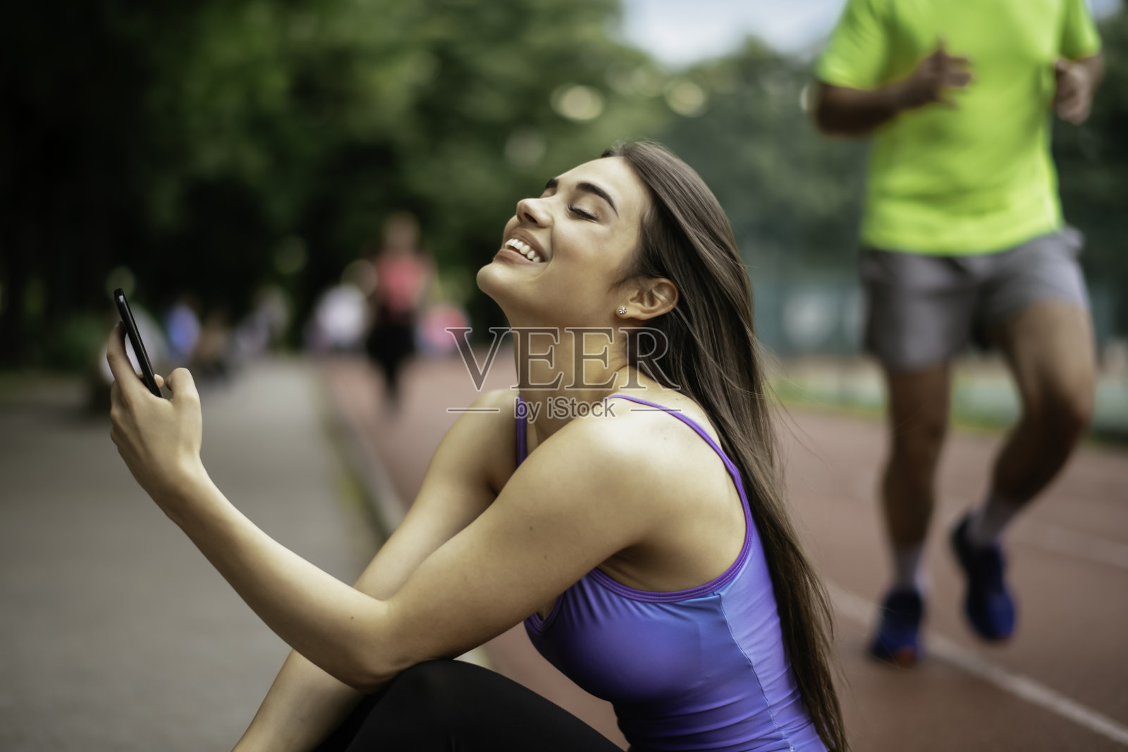 年轻的女运动员坐在长椅上打电话。照片摄影图片
