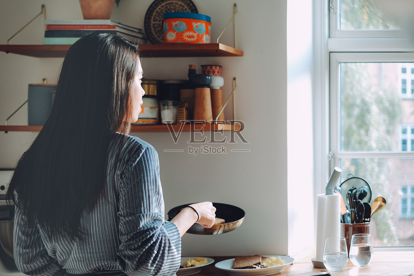 微笑的亚洲年轻女子在厨房做早餐在家。照片摄影图片