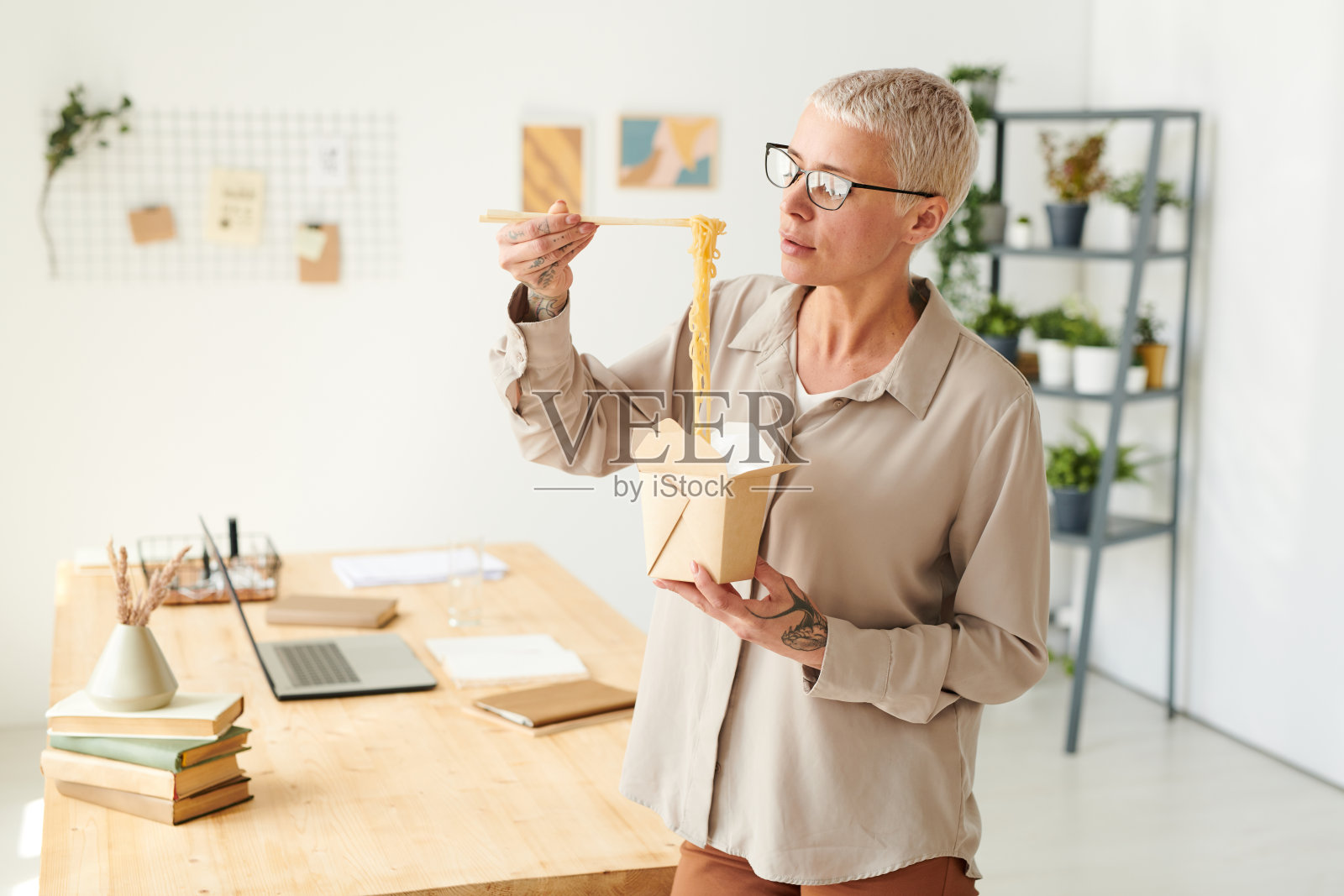 饥饿美丽的女商人戴着眼镜在办公室吃午饭的时候吃盒装面条照片摄影图片