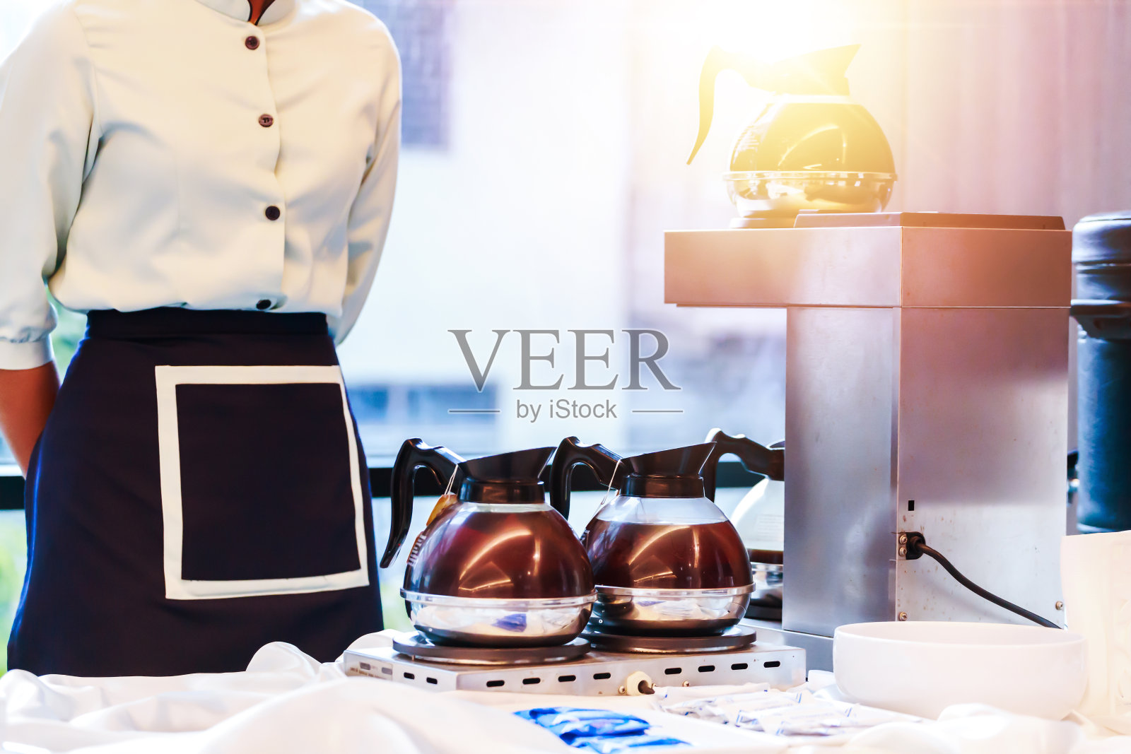 服务员站在煤气炉和咖啡机里的咖啡杯旁边。照片摄影图片