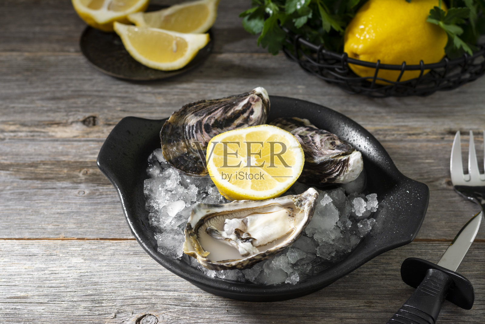 黑色盘子里的牡蛎和冰块放在灰色的木桌上。健康的海鲜照片摄影图片