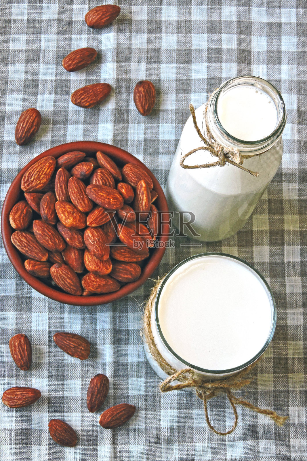 杏仁牛奶装在玻璃瓶里,杏仁装在碗里。照片摄影图片