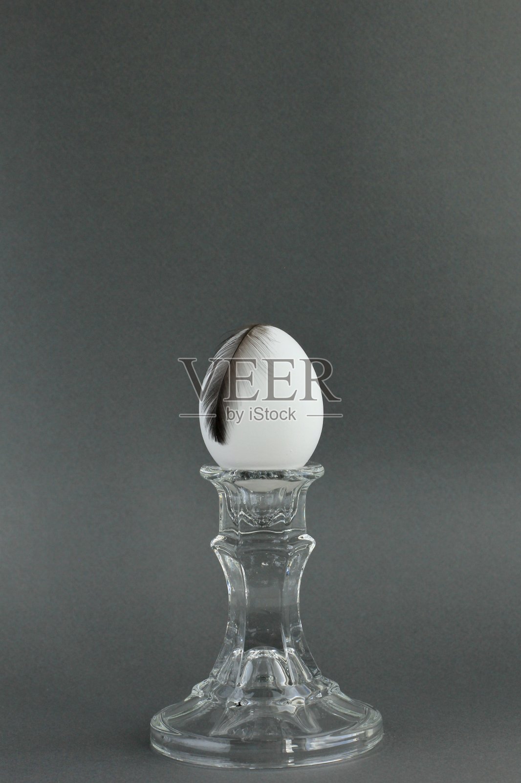 一个白色的鸡蛋放在一个古典的玻璃烛台上,带有纹理的灰色背景和阴影。创意简约的现代食品理念,复活节。照片摄影图片