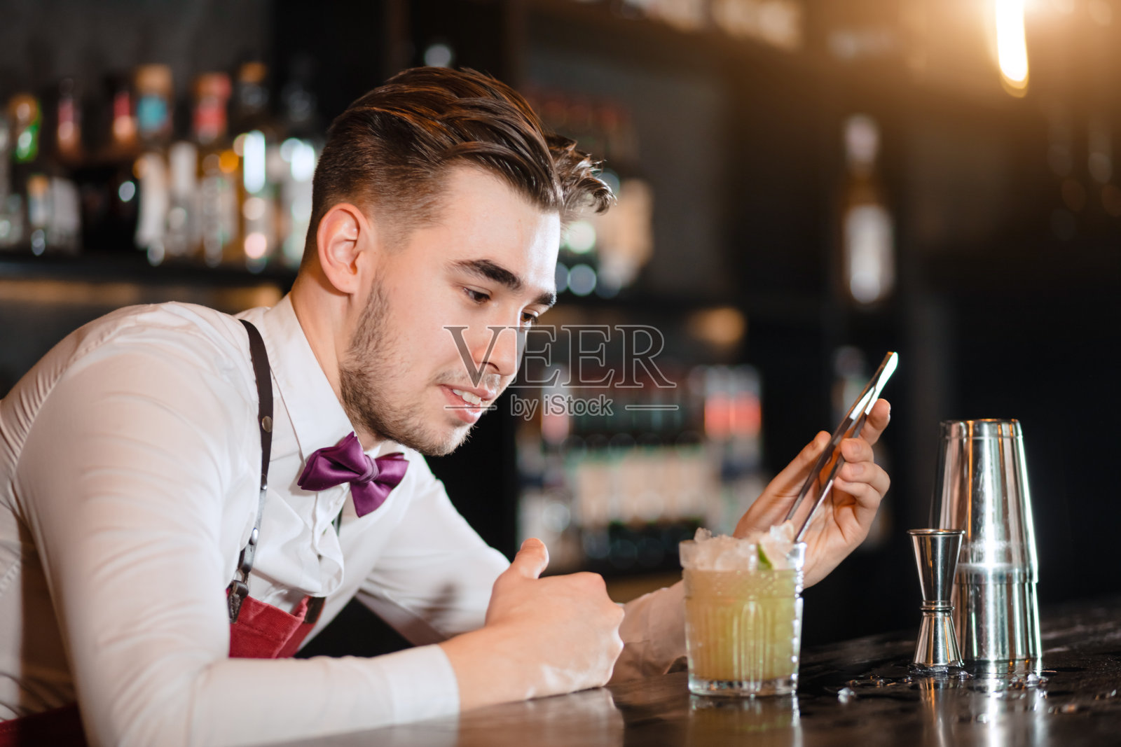 调酒师用镊子夹上一片酸橙装饰鸡尾酒。照片摄影图片