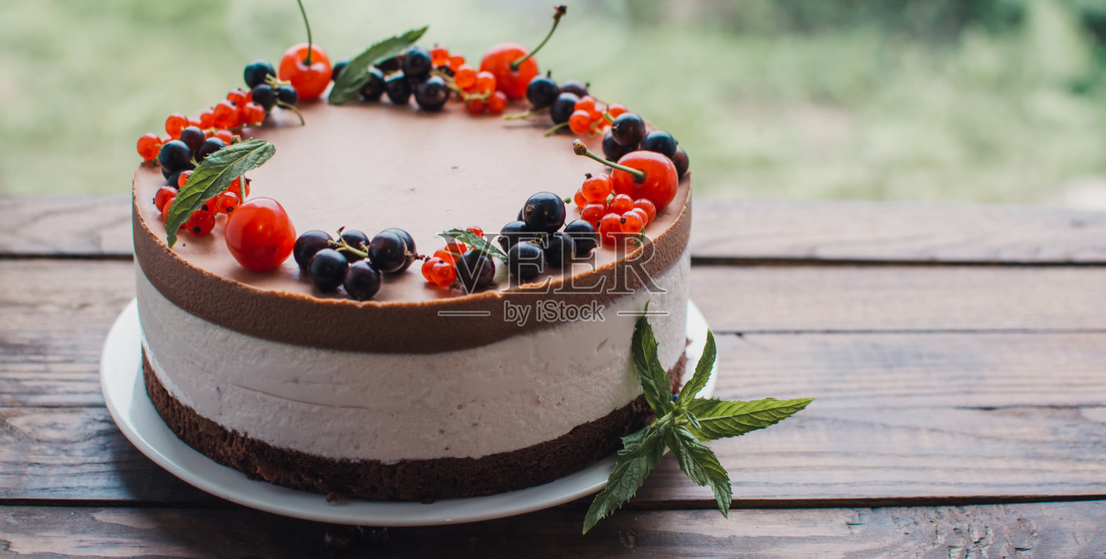 木桌子上有浆果的慕斯蛋糕。巧克力奶油蛋糕加醋栗和樱桃。生日、婚礼和其他节日的浆果蛋糕。照片摄影图片