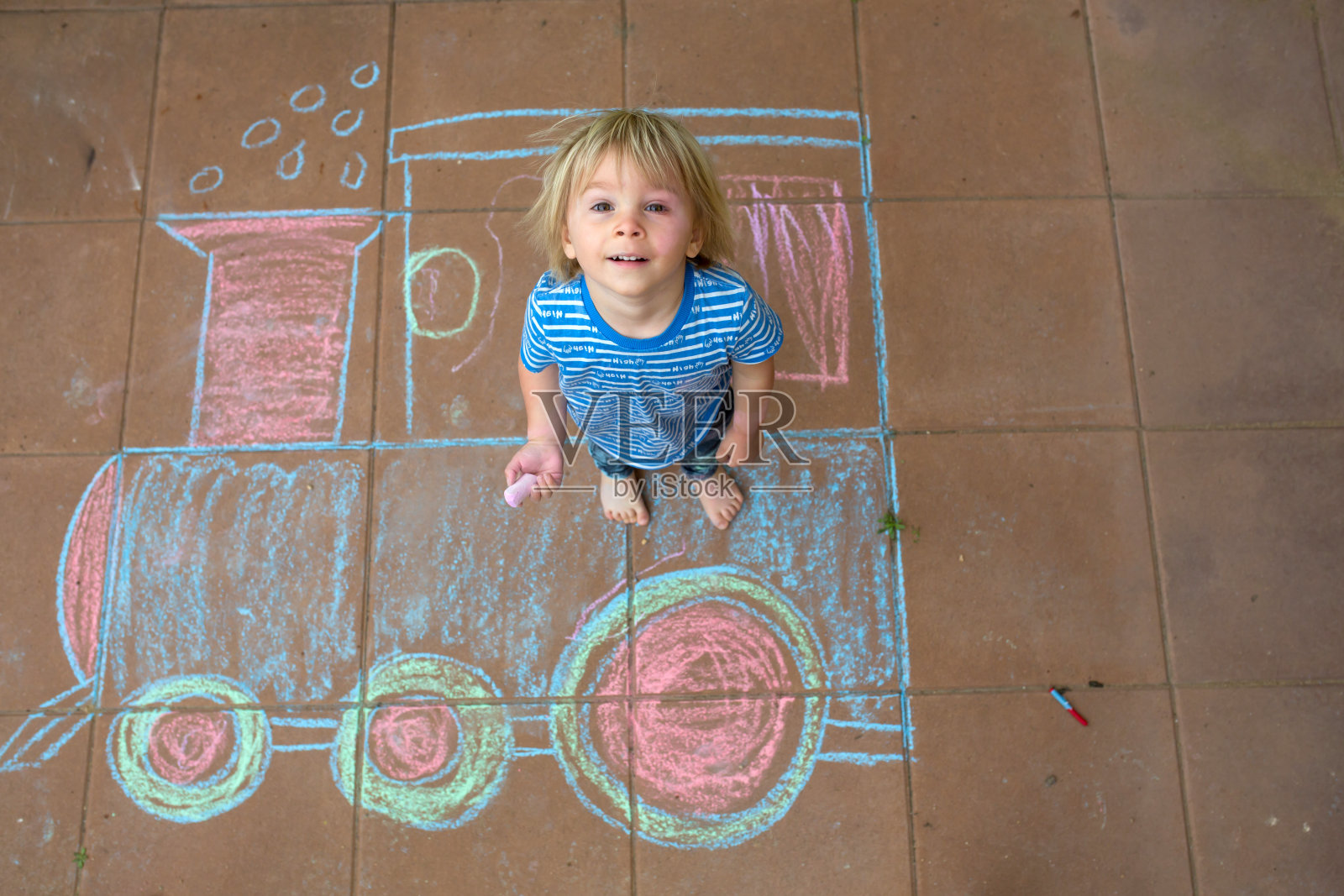 可爱的学步男孩,玩粉笔,在人行道上画画,坐火车,躺在地上照片摄影图片