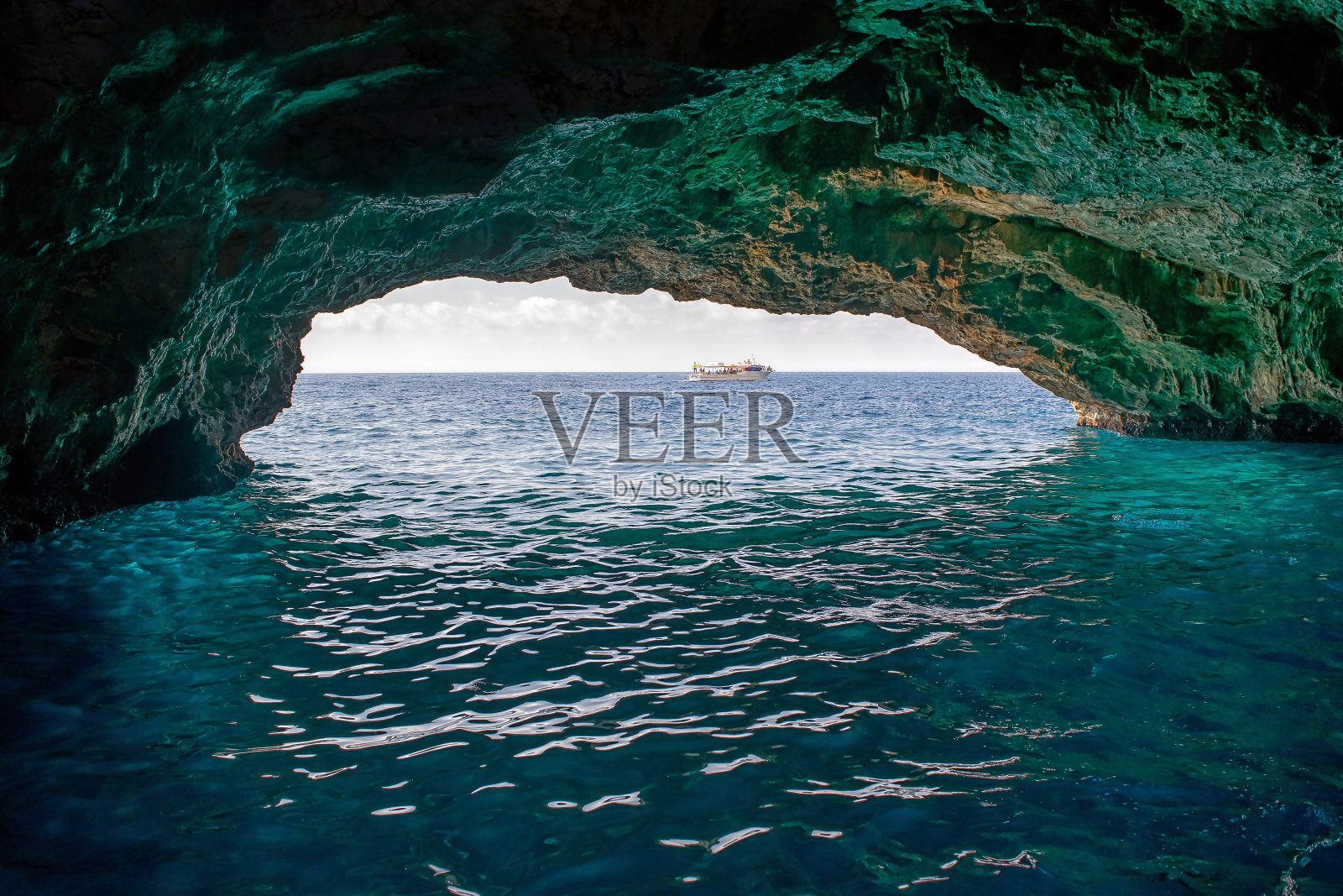 石洞里蓝色的海水,地平线上有一条小船,隧道尽头有光照片摄影图片