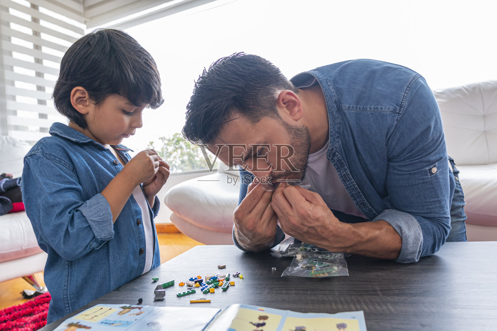 父亲和儿子在客厅的桌子上玩,他们收集了一个玩具,穿一样的衣服照片摄影图片