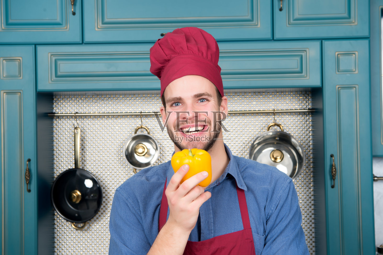 戴厨师帽的家伙微笑着在厨房里放黄辣椒照片摄影图片
