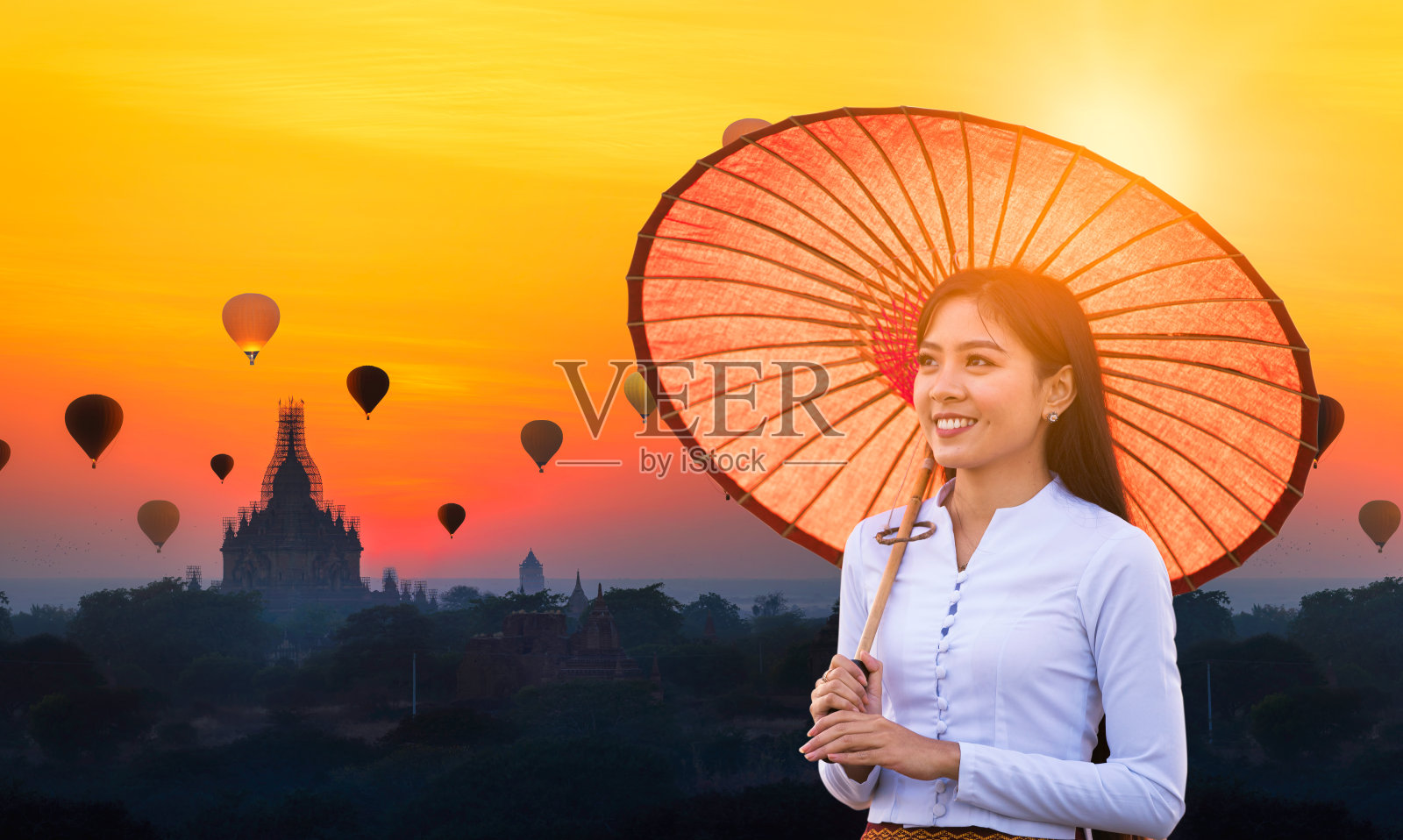 一位年轻的缅甸妇女拿着一把红伞走着。在缅甸蒲甘,年轻的女孩和日出许多热气球与佛塔。空间的文本。照片摄影图片