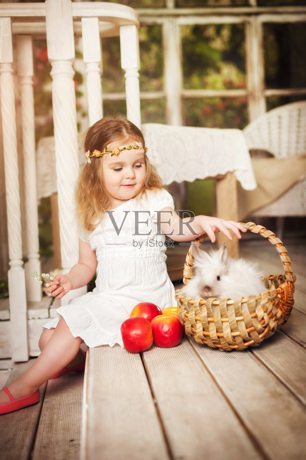 一个可爱的小女孩和一只白兔的肖像。一个小孩在阳台上玩兔子。一只兔子坐在篮子里。复活节庆祝活动。婴儿和动物的概念。春天的花园。照片摄影图片