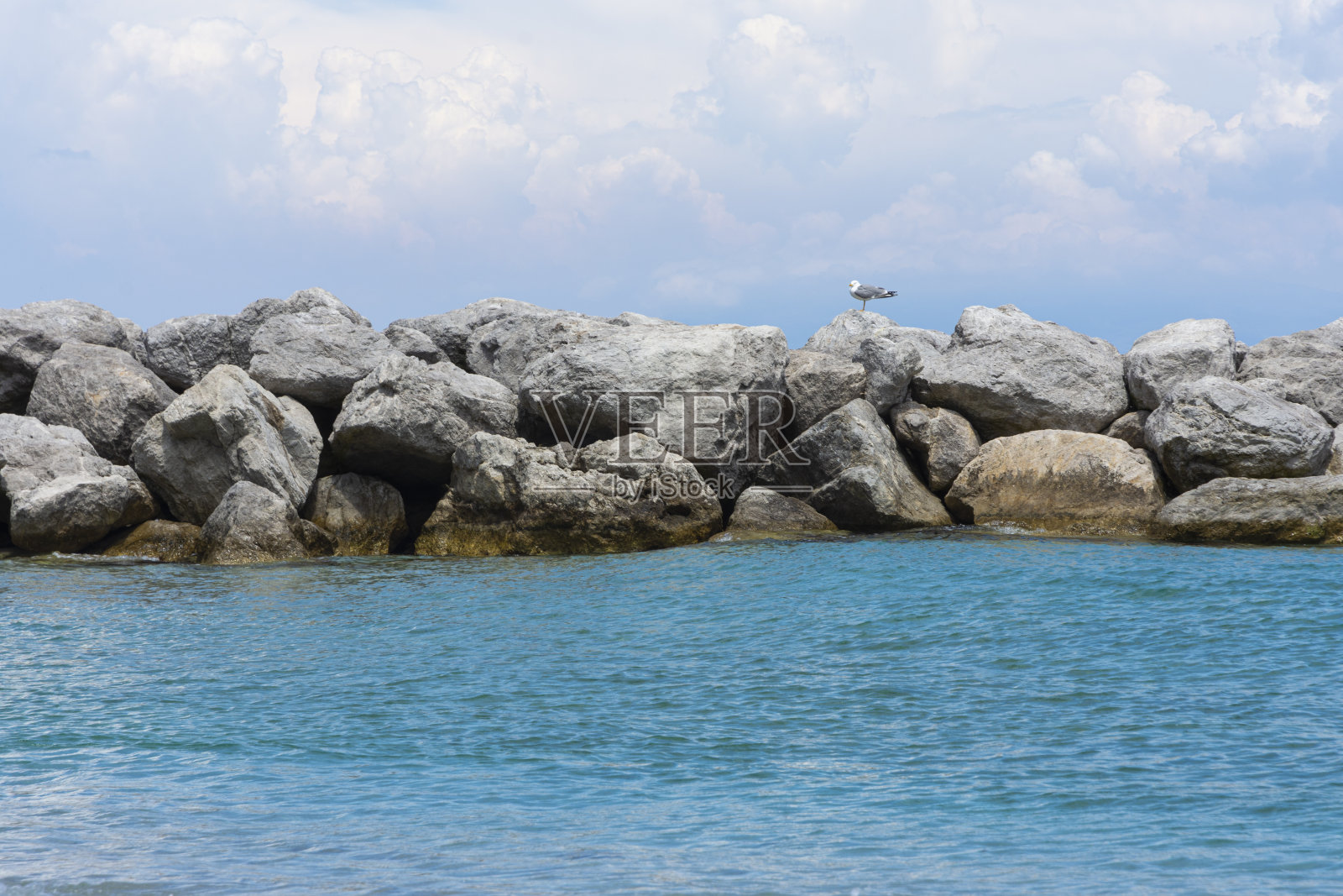 А海上的石头墙,一只海鸥栖息在上面。照片摄影图片