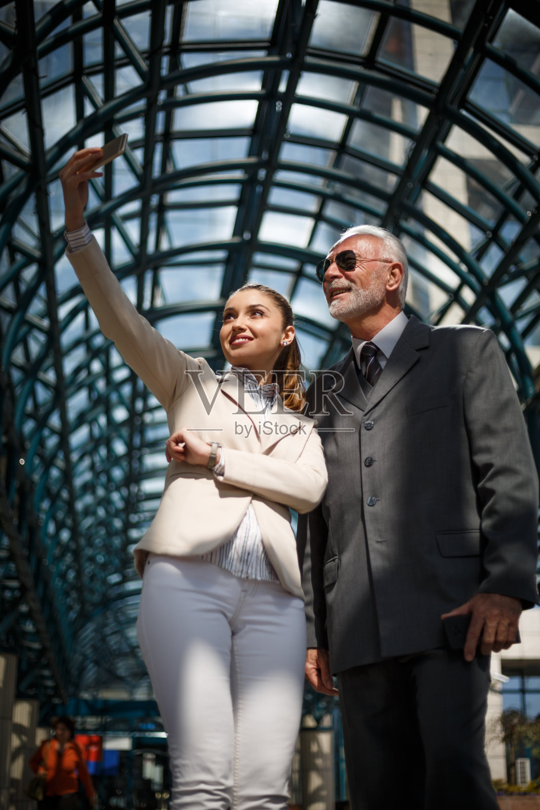 一位年长的商人穿着优雅的西装和他年轻漂亮的助手在工作间隙自拍照片摄影图片