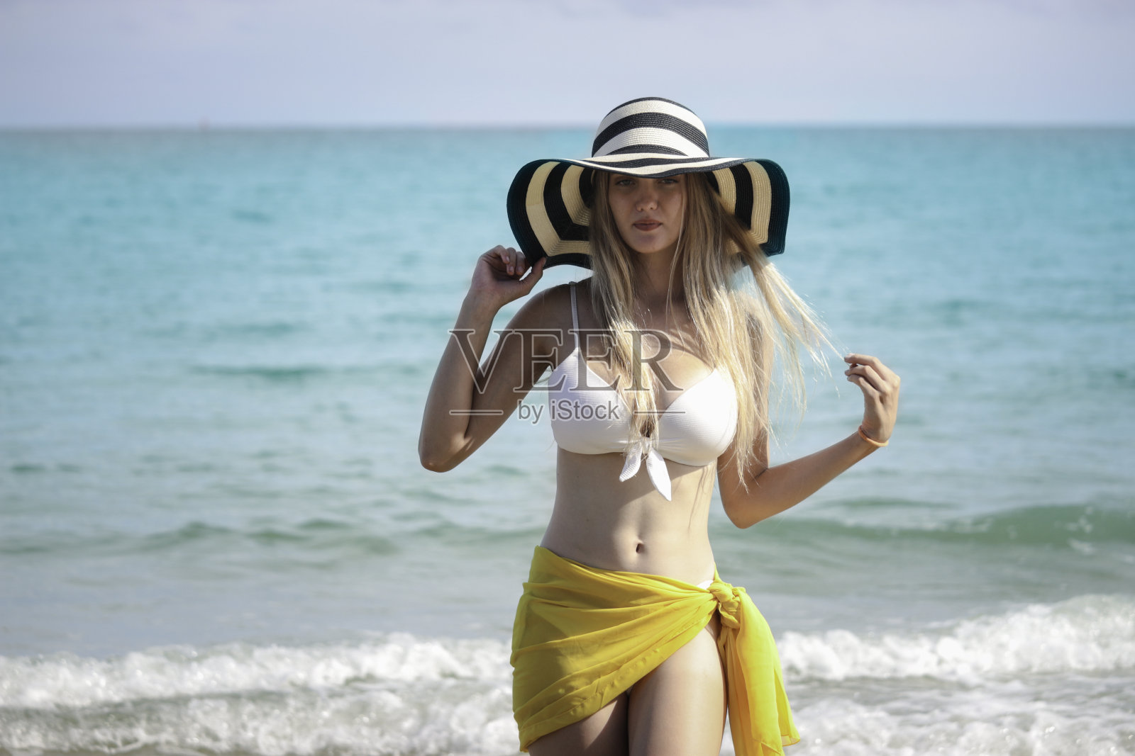 快乐的暑假,性感美丽的金发美女穿着白色的比基尼和帽子与黄色的披肩在海滩上玩耍,休息和花时间放松在蓝色的海洋热带岛屿照片摄影图片