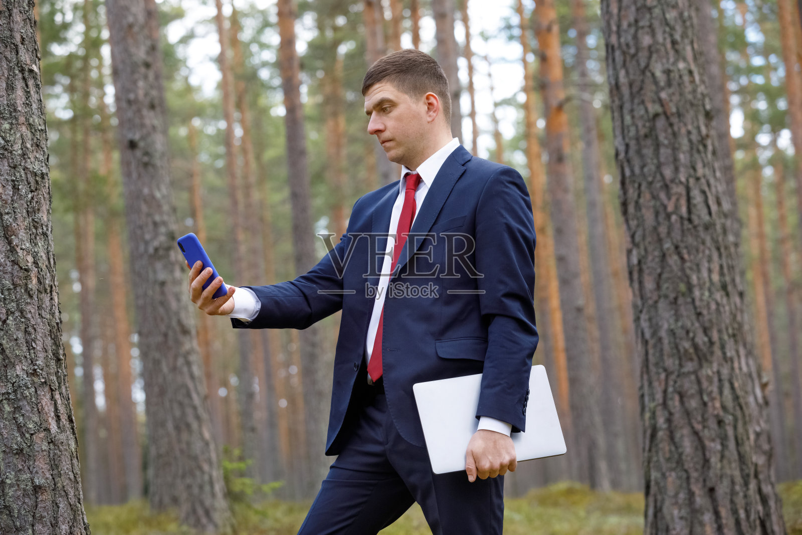 一个穿着西装在树林里拿着笔记本电脑的人。商人在视频聊天的本质。在一个阳光明媚的夏日远程工作。照片摄影图片