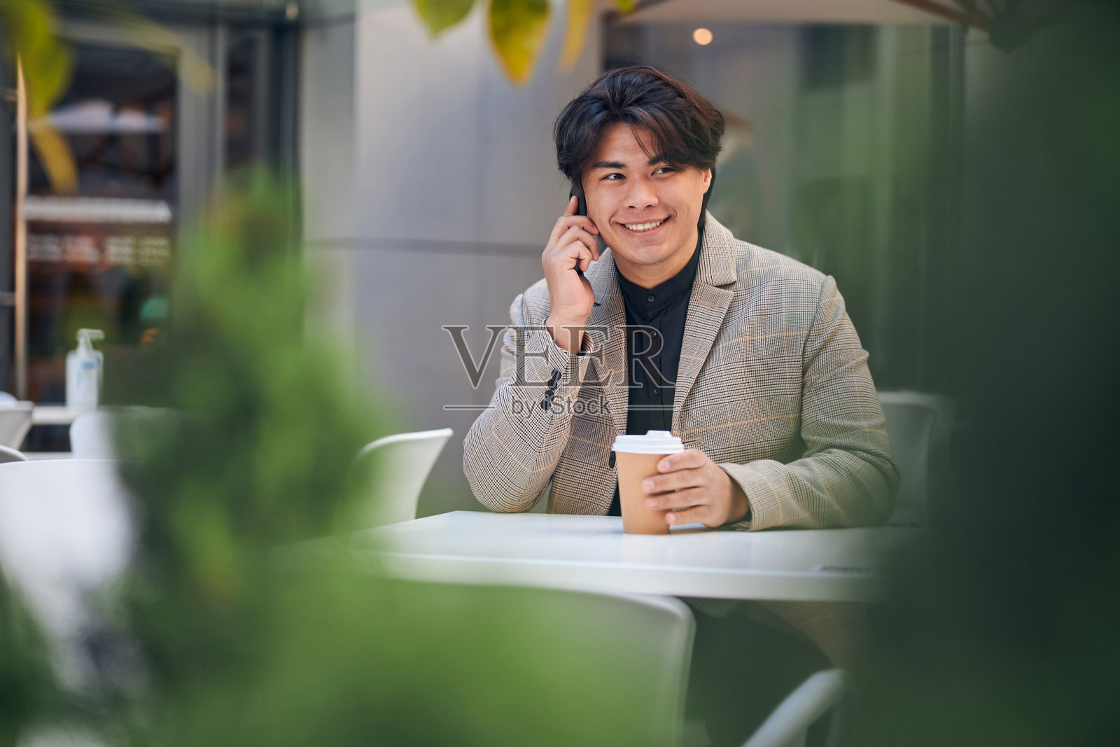 一个愉快的年轻人在户外的咖啡馆里打电话照片摄影图片