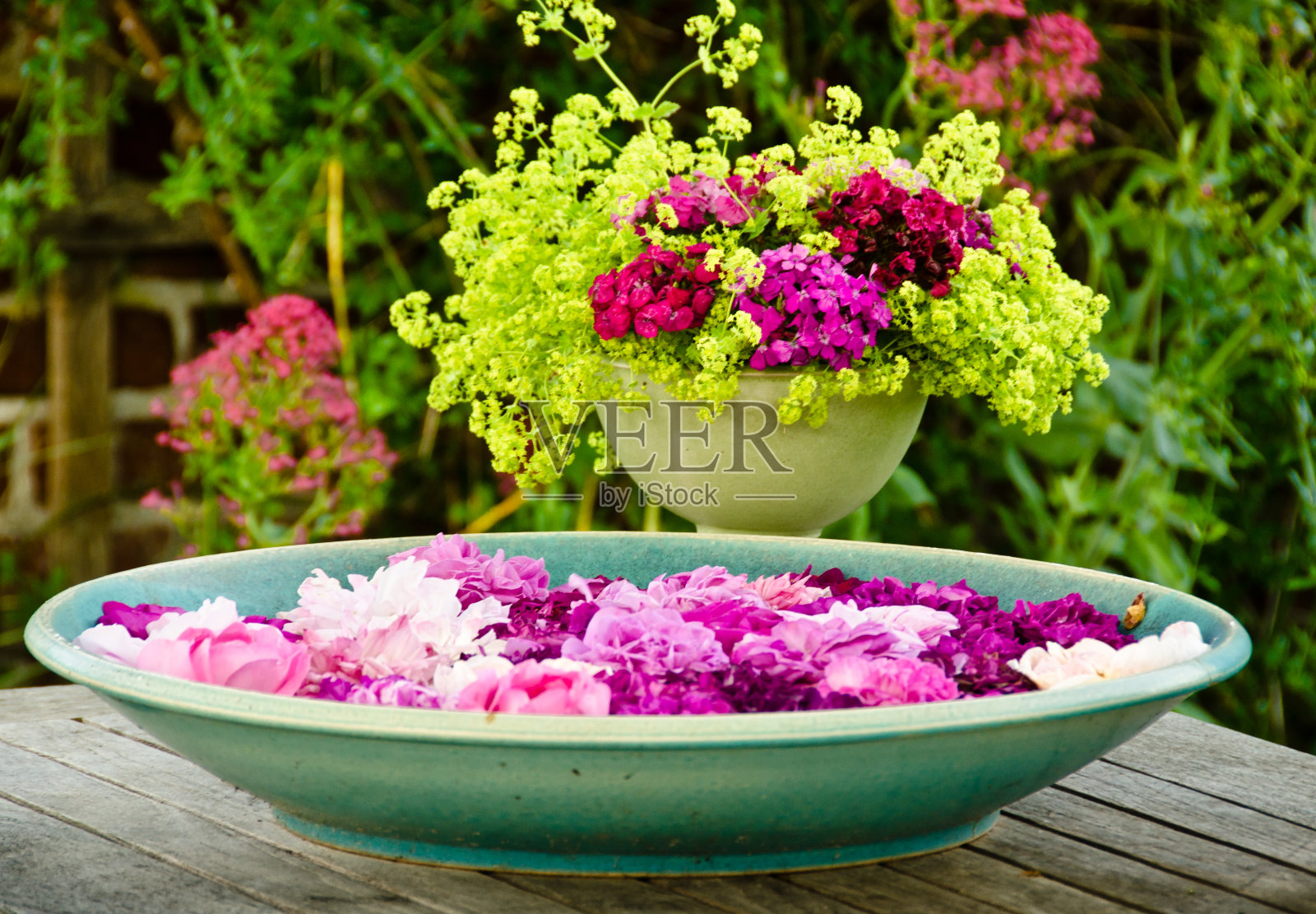 在花园里的一张木桌上放着一大堆盛满水的陶罐和许多粉红色花朵的叶子,前面是一束美丽的鲜花照片摄影图片