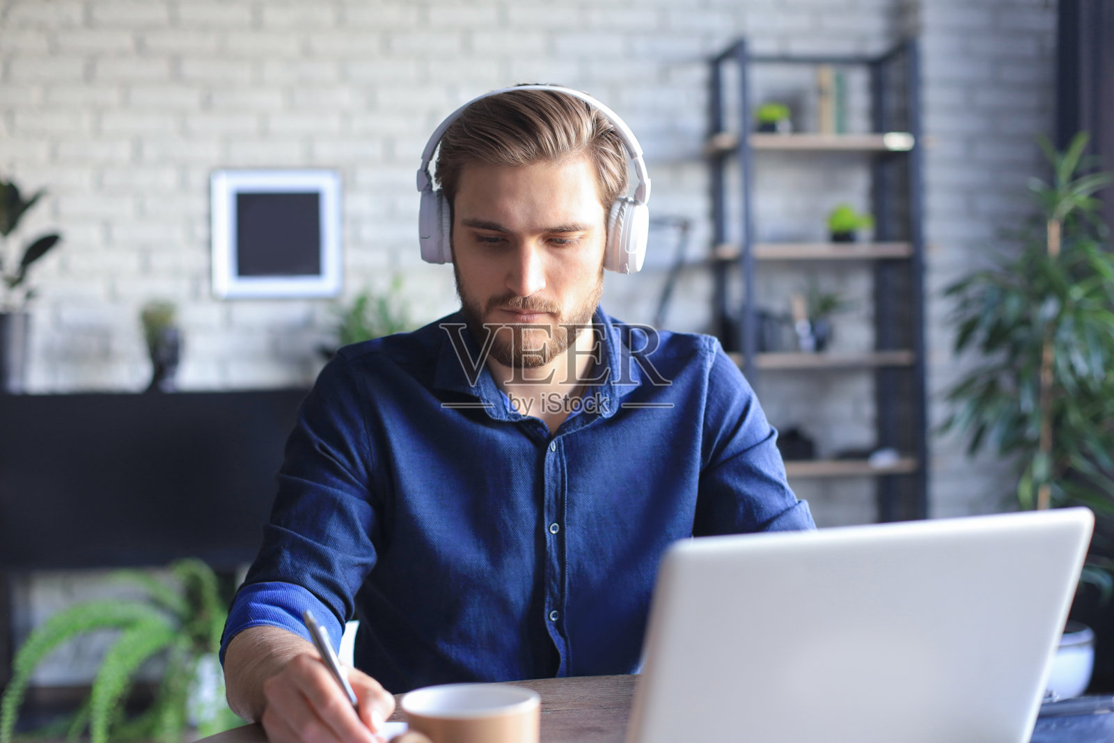 信心十足的商人戴着耳机坐在家里用笔记本电脑写笔记或财务报告。照片摄影图片