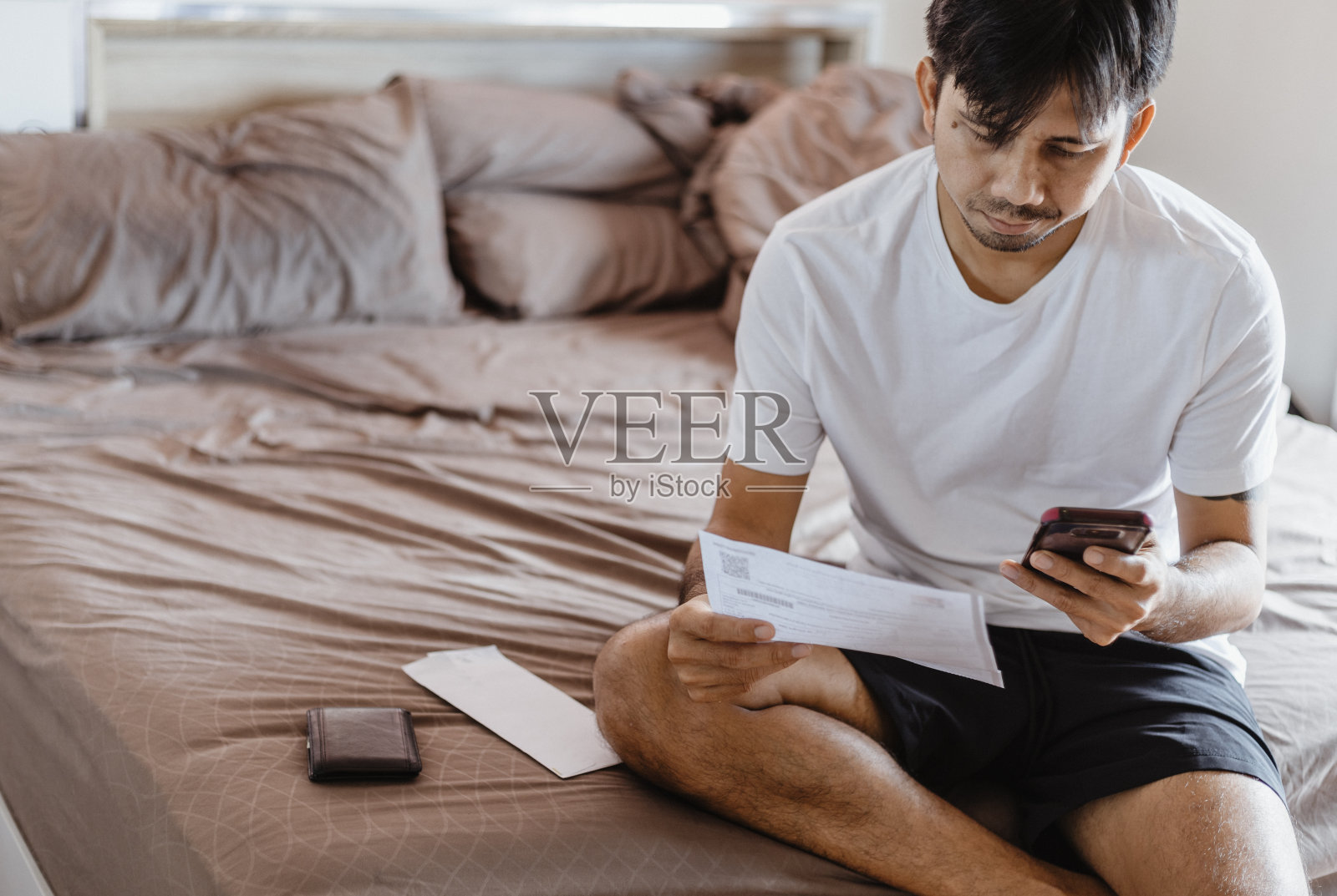 亚洲人在卧室里收到发票后会使用智能手机计算付款。网上付款的概念照片摄影图片