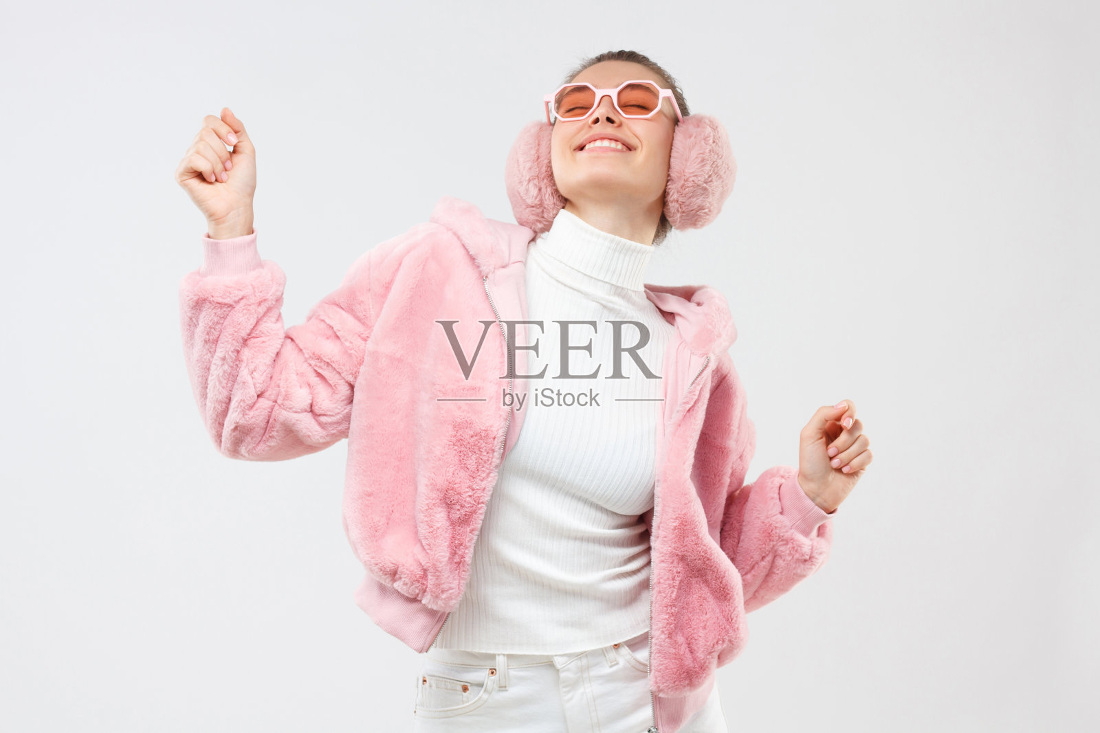 年轻的女性穿着粉红色的时髦服装,挥动手臂,微笑着,在派对上随着音乐的声音跳舞,享受着她的空闲时间,在灰色的背景下孤独照片摄影图片