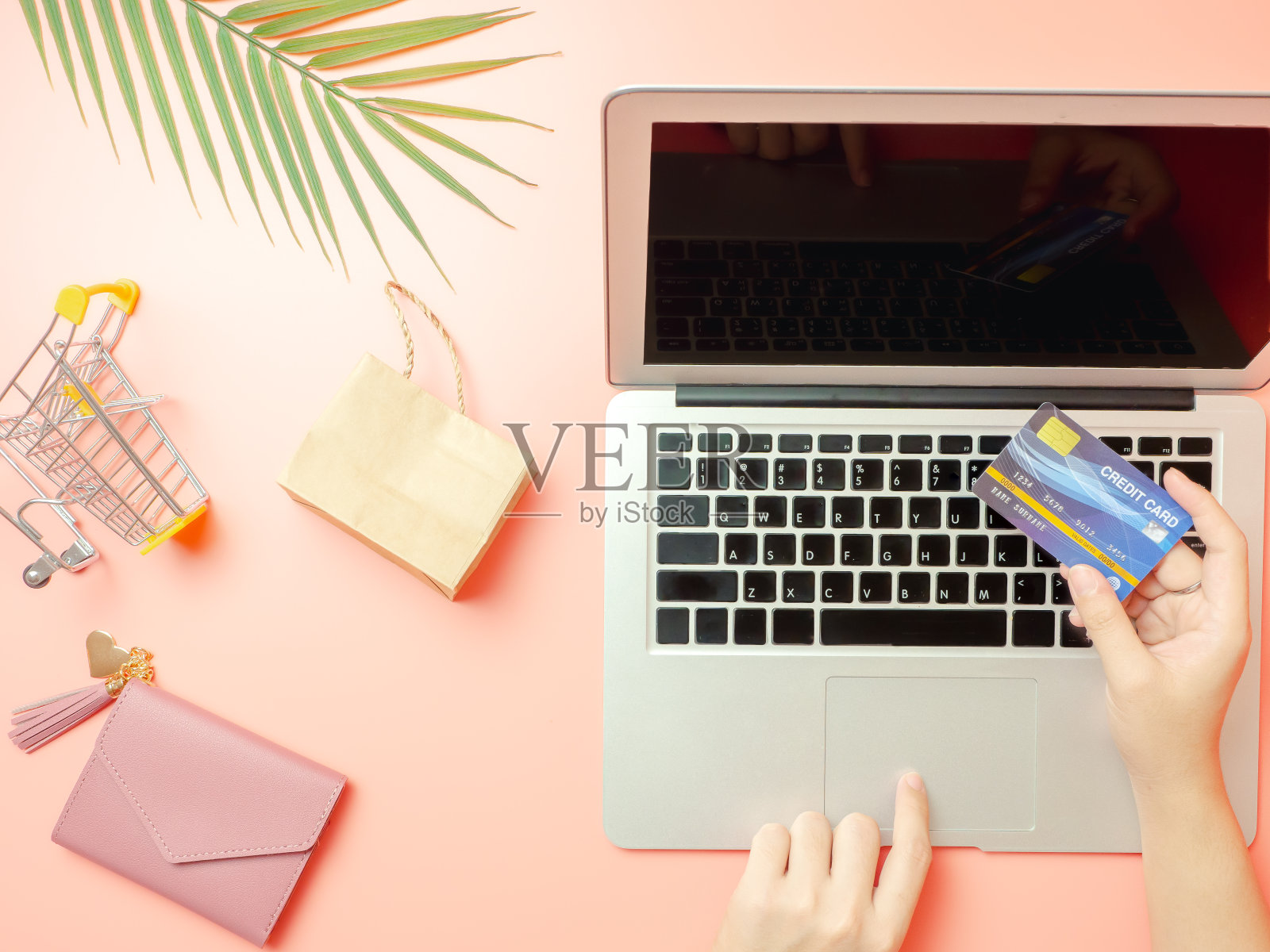 夏天购物和网上支付概念从女人拿着粉红色的钱包与信用卡和使用笔记本电脑在粉粉背景在线支付。俯视图照片摄影图片