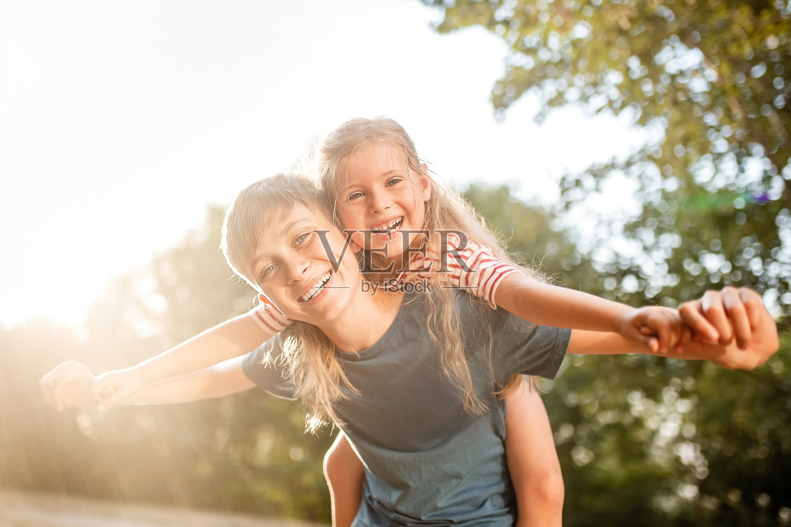 快乐的孩子们男孩和女孩在公园里嬉戏。在一个夏日的夕阳下,哥哥和妹妹在大自然中玩耍。照片摄影图片