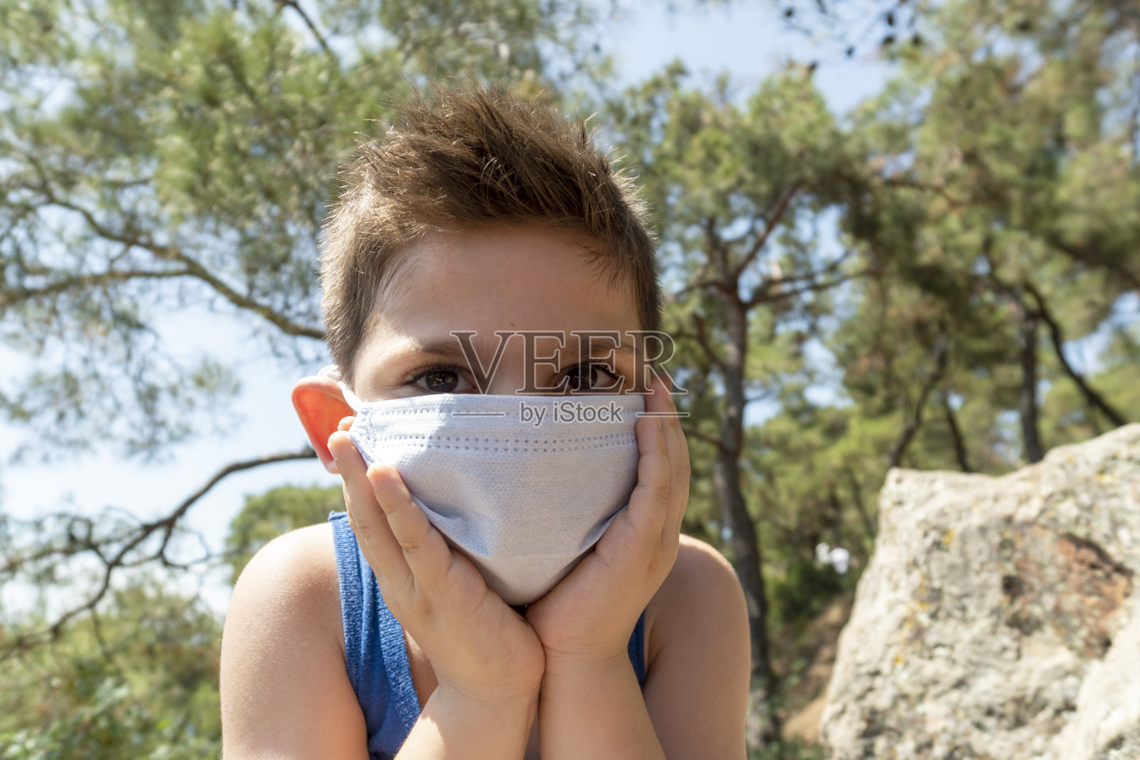 为了躲避新冠肺炎,一名男孩戴着医用口罩,试图接受阳光照射照片摄影图片
