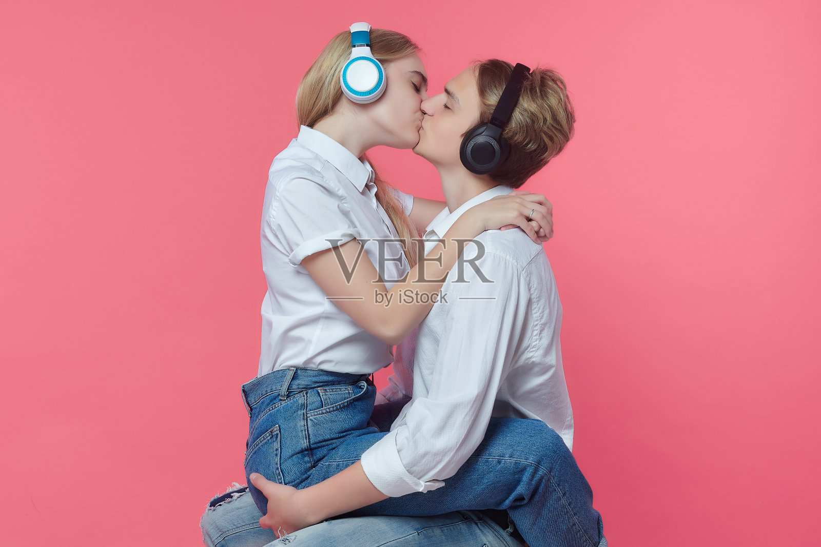 男孩和女孩戴着耳机。一边听音乐一边用一个吻来表达情感。粉红色的背景照片摄影图片
