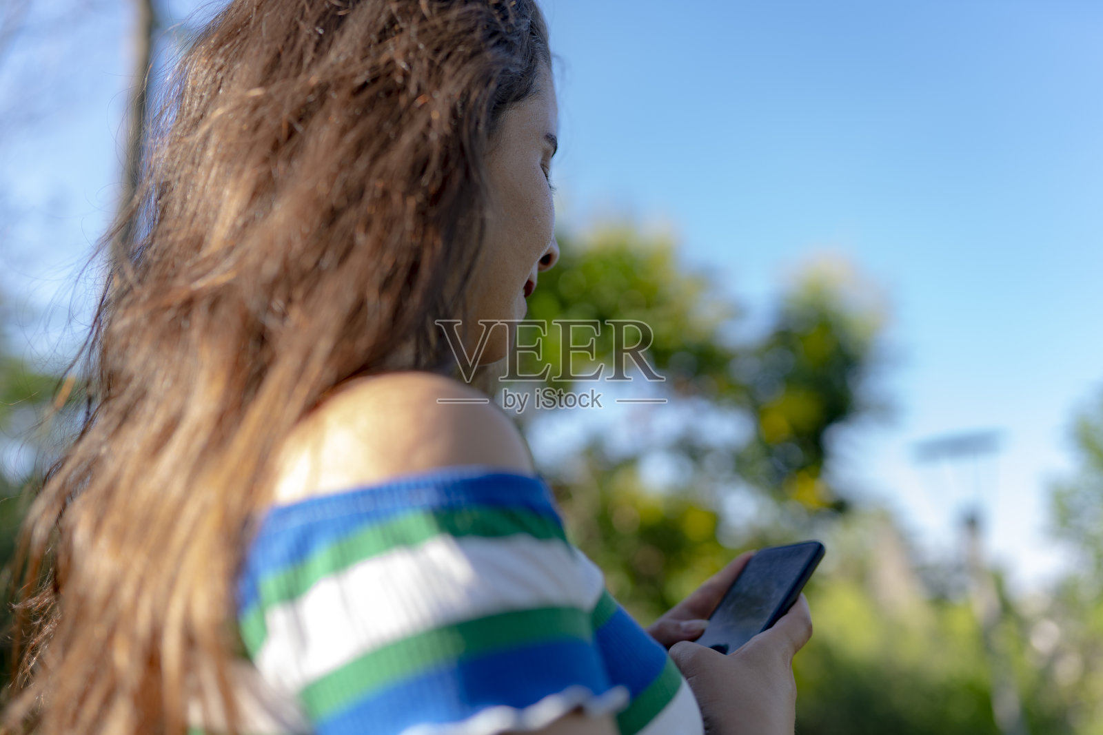 微笑女孩的肖像在伟大的心情,休息在城市花园。将模型的侧面转向相机,看手机屏幕照片摄影图片