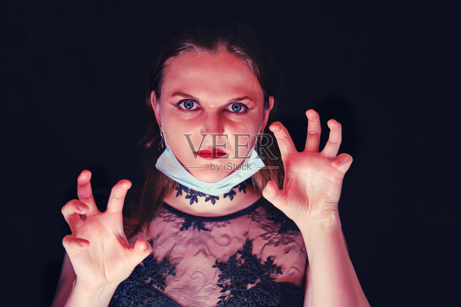 一个带着医用面具的吸血鬼女人的愤怒表情。在冠状病毒流行期间,女孩化妆吸血鬼万圣节。照片摄影图片