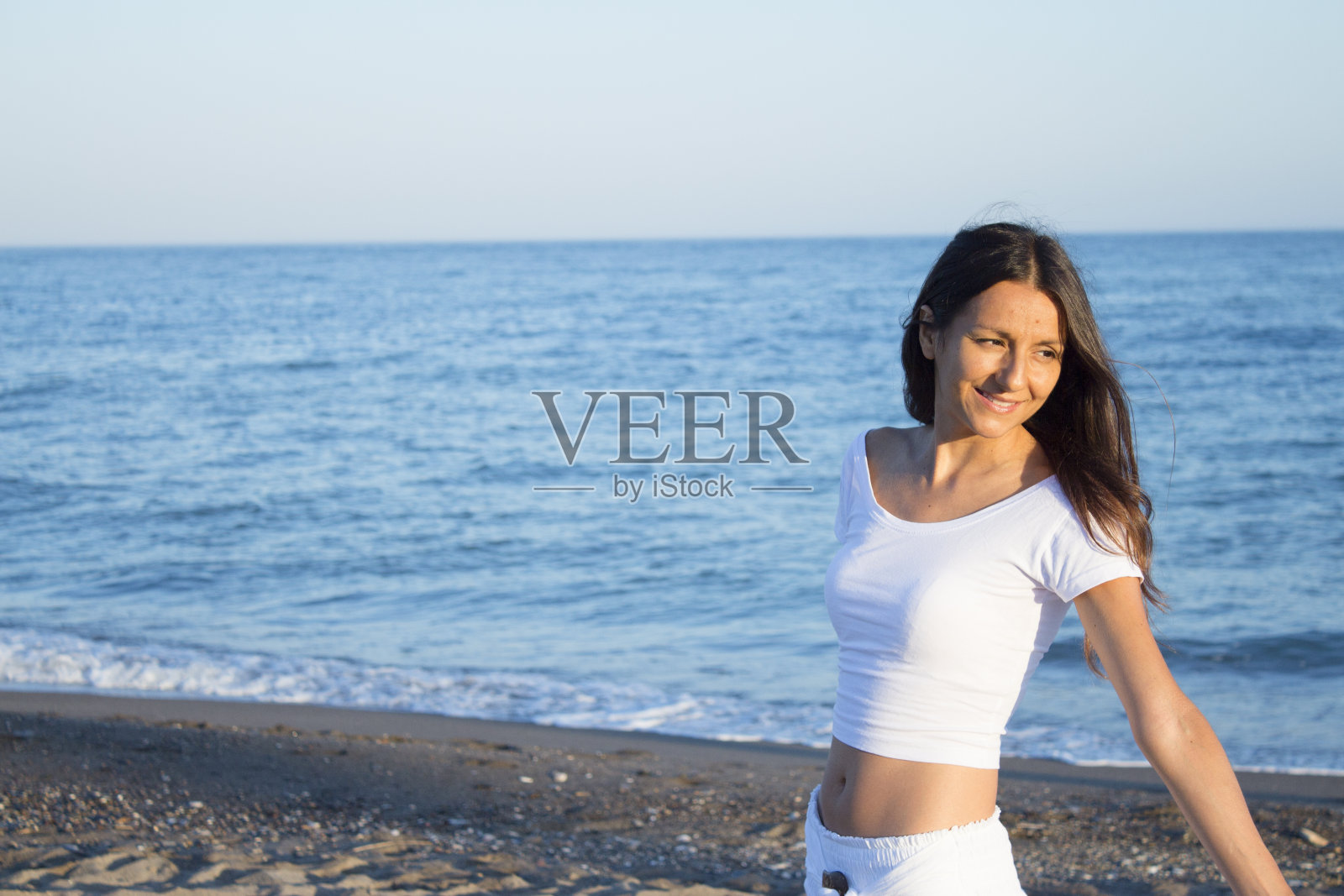 穿着白色衣服的女人赤脚躺在沙滩上。微笑照片摄影图片