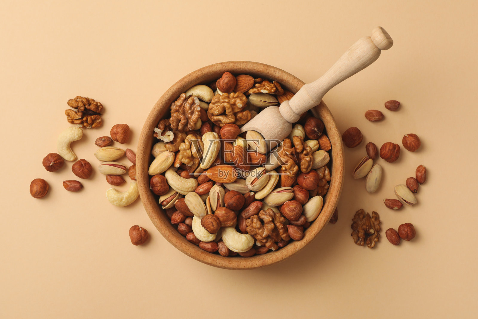 碗与不同的坚果和木勺米色背景照片摄影图片