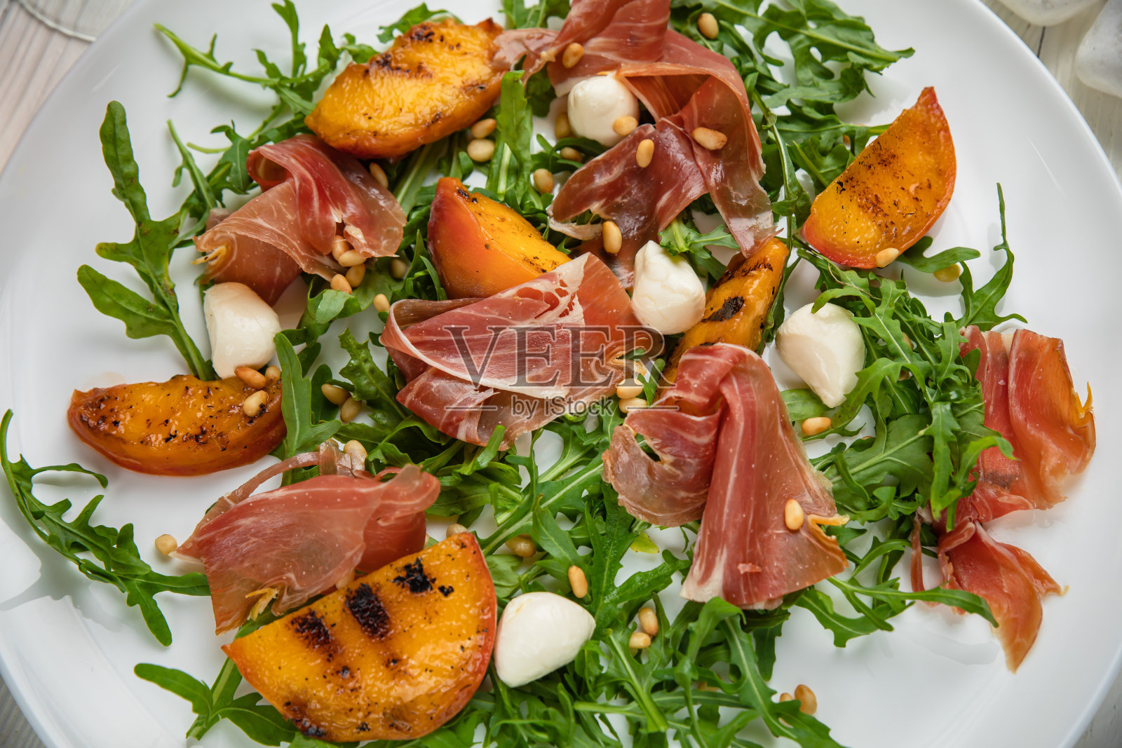 白色盘子上放有芝麻菜和桃子的火腿照片摄影图片