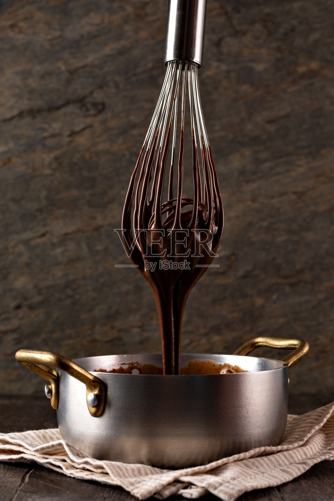 液态巧克力奶油从搅拌器倒入勺子。照片摄影图片